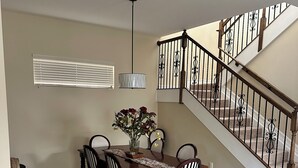 Un comedor con una mesa, sillas y un florero. Se ve una escalera con barandilla que sube a un nivel superior.