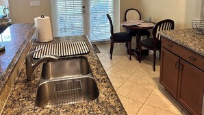 Una cocina con encimeras de granito, un lavaplatos de acero inoxidable, una zona de comedor con mesa y sillas, y una puerta corrediza de vidrio que da a un patio.