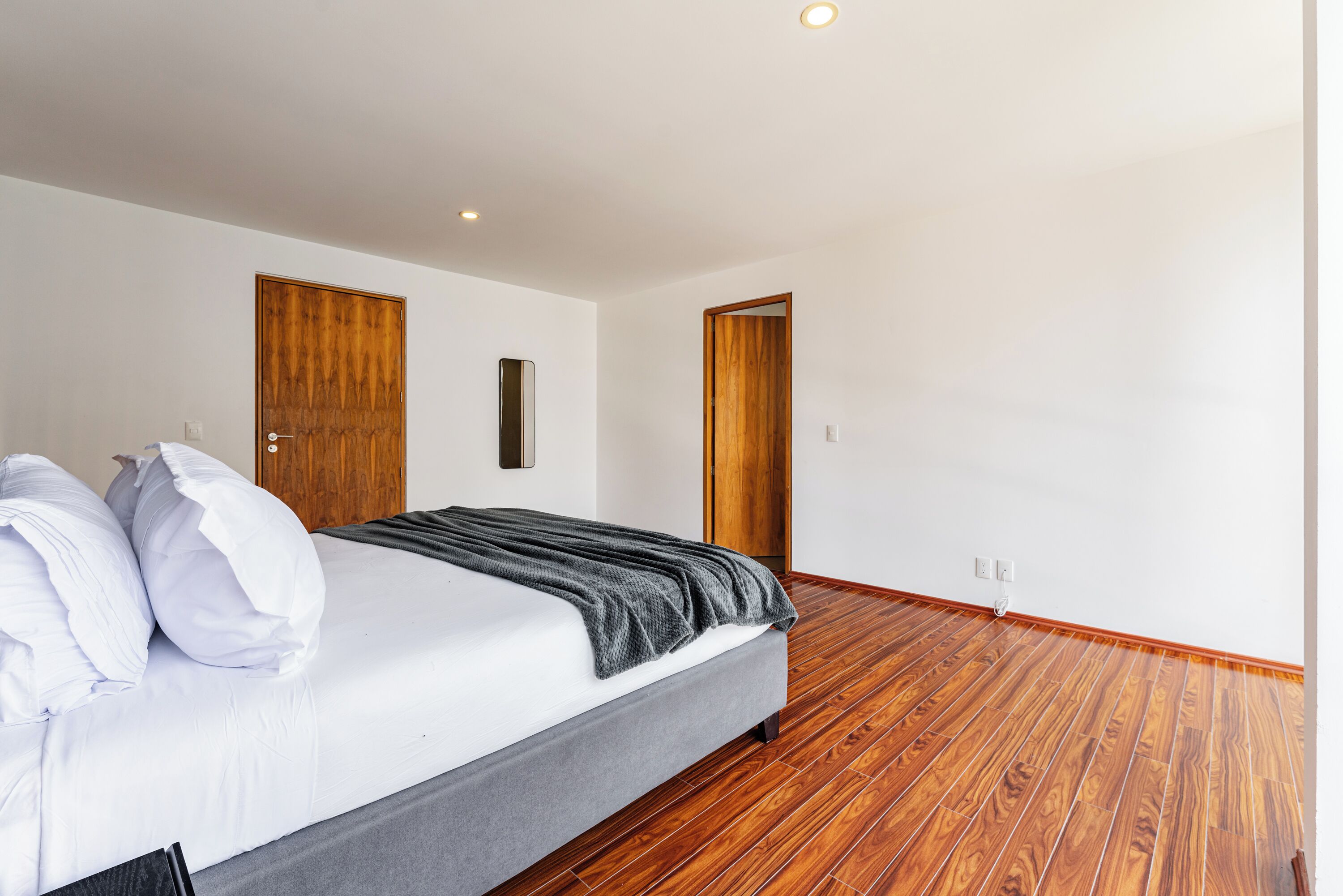 A bedroom with a bed, wooden flooring, and two wooden doors.