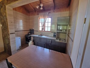 Una cocina compacta con techo de madera, refrigerador, estufa, pileta y ventana con cortinas.