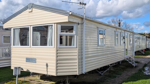 Ein Caravan namens 'Darwin Deluxe' mit flachem Dach, großen Fenstern und einer Satellitenschüssel.
