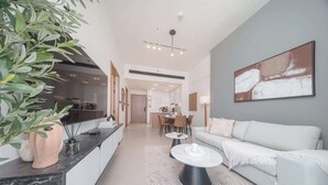 Uma sala de estar moderna com um sofá branco, uma mesa de centro e uma área de jantar ao fundo.
