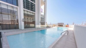 Piscina interna com água azul cristalina, rodeada por um muro de vidro e um deck revestido de azulejos brancos.