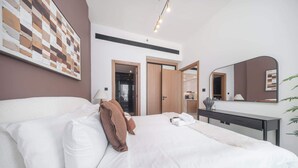 Quarto de hotel moderno com uma cama grande, uma escrivaninha, um espelho e vista para o banheiro.