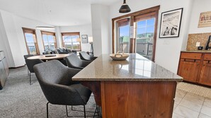 A modern kitchen with a granite countertop, dark chairs, and a wooden cabinet. - Soaring Eagle Lodge #217 Beautiful upgraded Corner Unit Wraparound Balcony Ski-in/Ski-out Underground parking (Snowshoe)