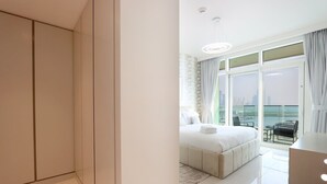 A modern hotel room with a large bed, a balcony with a city view, and a separate seating area.