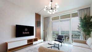 A modern living room with a flat-screen TV mounted on the wall, a sofa, a coffee table, and a large window offering a city view.