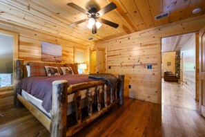A log cabin bedroom with a bed, a ceiling fan, and a painting on the wall.