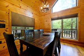A wooden interior with a large dining table, chairs, and a chandelier.