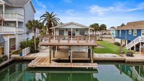 Een huis aan het water met een houten terras, een zwembadje en een gazon.