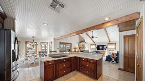 A spacious kitchen with a large island, wooden cabinets, and a high ceiling with exposed beams. - Reelview by Ryson Vacation Rentals (Galveston)