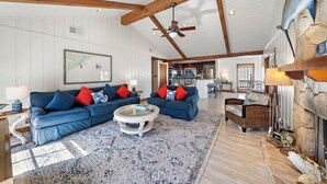 A spacious living room with a large blue sectional sofa, a round coffee table, and a stone fireplace. - Reelview by Ryson Vacation Rentals (Galveston)