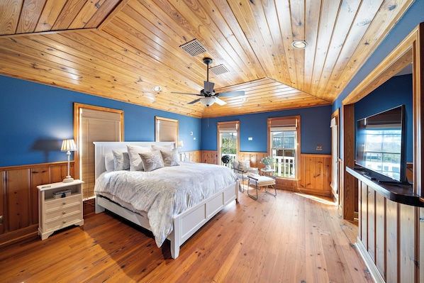 Une chambre avec un plafond en bois, un grand lit, une table de chevet, une chaise et une fenêtre.