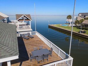 A wooden deck with a table and chairs, a covered seating area, and a view of a calm body of water. - Reelview by Ryson Vacation Rentals (Galveston)