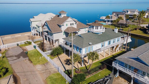 A large, multi-story house with a prominent tower, situated by a calm body of water. - Reelview by Ryson Vacation Rentals (Galveston)