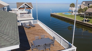 A wooden deck with a table and chairs, a covered seating area, and a view of a calm body of water. - Reelview by Ryson Vacation Rentals (Galveston)