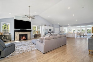 A spacious living room with a fireplace, a grey sofa, and a dining area with a view.