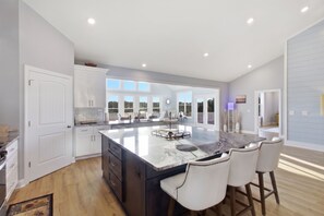 A modern kitchen with a large island, white cabinetry, and a view to the outside.