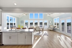A spacious kitchen with a large island, dining area with chairs, and a view of the outdoors through large windows.