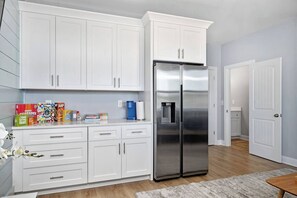 A modern kitchen with white cabinetry, a stainless steel refrigerator, and a variety of breakfast cereals on the counter.