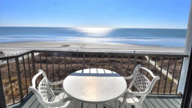 Ein Balkon mit Tisch und Stühlen mit Blick auf einen Strand.