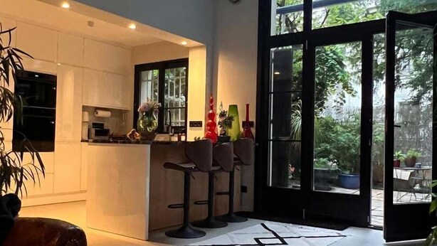 A modern kitchen with a large window, a dining area with a round table, and a bar area with stools.