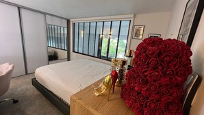 A bedroom with a bed, a wooden nightstand, a glass vase, and a red rose arrangement.