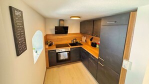 A compact kitchen with dark cabinets, a wooden countertop, a built-in oven, and a black range hood. - Lovely Old Town Studio (Hall in Tirol)