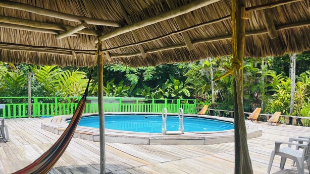 A wooden deck with a pool, surrounded by green foliage and a thatched roof. - 3-Bedroom house, air-conditioned, private kitchen, private bathroom, living  room and a private garden. (Cayo)