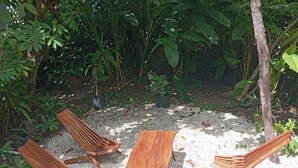 A patio with wooden furniture and a gravel surface surrounded by dense foliage. - 3-Bedroom house, air-conditioned, private kitchen, private bathroom, living  room and a private garden. (Cayo)