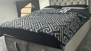 Een slaapkamer met een gestoffeerd hoofdeinde, een bedovertrek met een geometrisch patroon en een grijs vloerkleed.