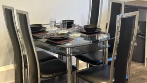 Een eettafel met vier stoelen, een glazen blad en enkele borden en glazen.