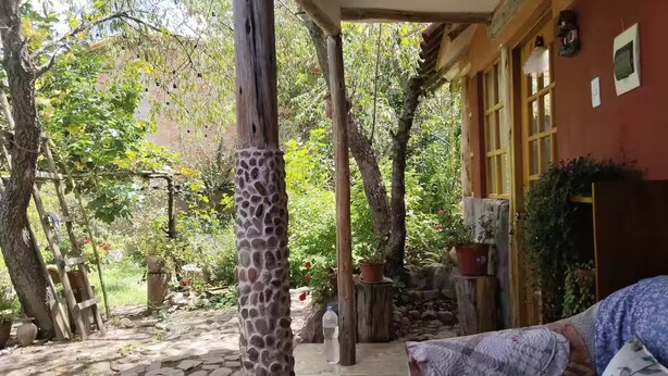 Un espacio al aire libre techado, con suelo de piedra, vigas de madera y plantas en macetas.