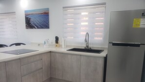 A kitchen with a stainless steel refrigerator, a sink, and a window with blinds.