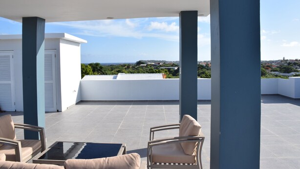 A rooftop terrace with outdoor seating, a view of the cityscape, and a clear sky.