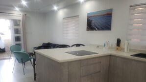 A modern kitchen with a central island, a dining area with chairs, and a large window with blinds.