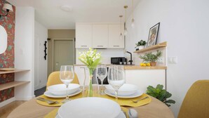 Een eetgedeelte met een ronde tafel gedekt voor twee personen, een bloevas en een keuken op de achtergrond.