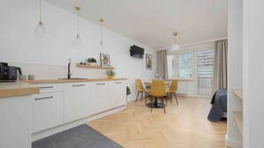 Een moderne keuken met witte kastjes, een houten aanrechtblad en hanglampen. Er is een eethoek met gele stoelen en een tafel.