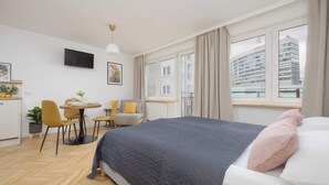 Een moderne hotelkamer met een groot bed, een bureau met stoelen, een televisie en een raam met uitzicht op de stad.