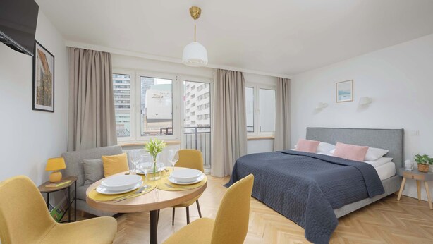 Een moderne hotelkamer met een bed, een zithoek met een tafel en stoelen, een bank en een balkon met gordijnen.