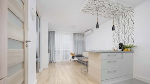 A modern kitchen with a wooden floor, a grey countertop, and a hanging pendant light. - Comfortable Apartment in the Center | View of Skyscrapers, Air Conditioning (Warszawa)