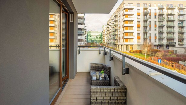 A balcony with wicker furniture, a glass door, and a view of high-rise buildings.