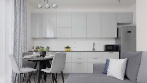 A modern kitchen with white cabinets, a dining area with grey chairs, and a grey sofa with decorative pillows.