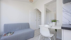A modern, minimalist room with a grey sofa, a white dining table with a chair, a small potted plant, and a marble backsplash. - Functional Apartment for 6 Persons | Air Conditioning, Balcony (Warszawa)