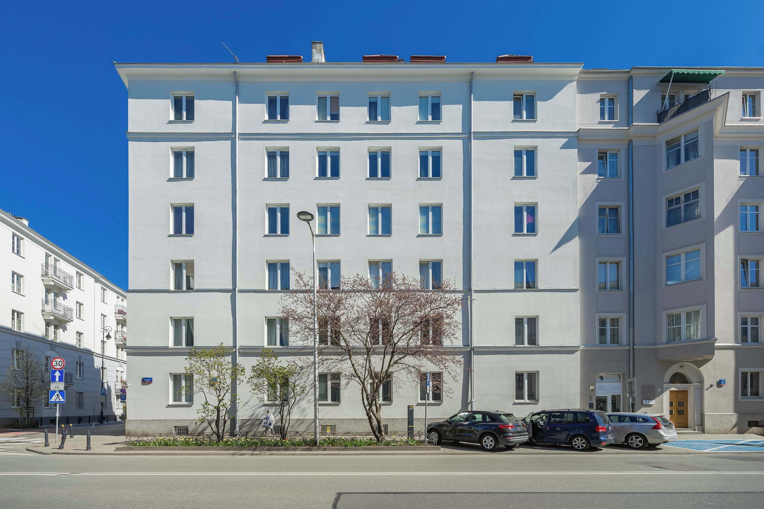 A multi-story building with a flat facade, several windows, and a parking area with cars.