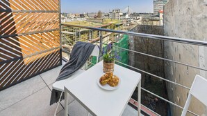Un balcón con una mesa blanca, una cesta de mimbre con una planta y un plato de pasteles.