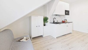 Una cocina compacta con armarios blancos, encimera negra y microondas.