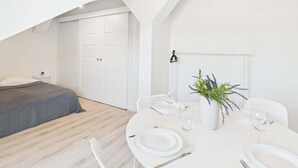 A modern, minimalist bedroom with a large bed, a white wardrobe, and a dining area with a round table set for two.