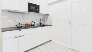 A modern kitchen with white cabinets, a black microwave, a stainless steel sink, and a marble backsplash.