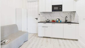 A compact kitchen with white cabinets, a black microwave, and a marble backsplash.